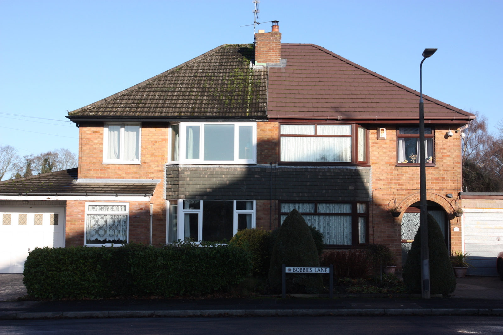 Bobbies Lane is in a green hedge in front of a semi detached house.
