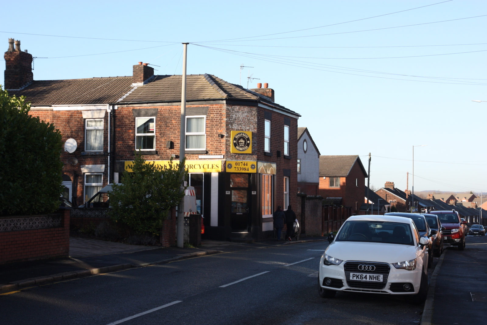Street Sign is photographed above a shop on a red brick building and isn't legible due to the sun shining on it.