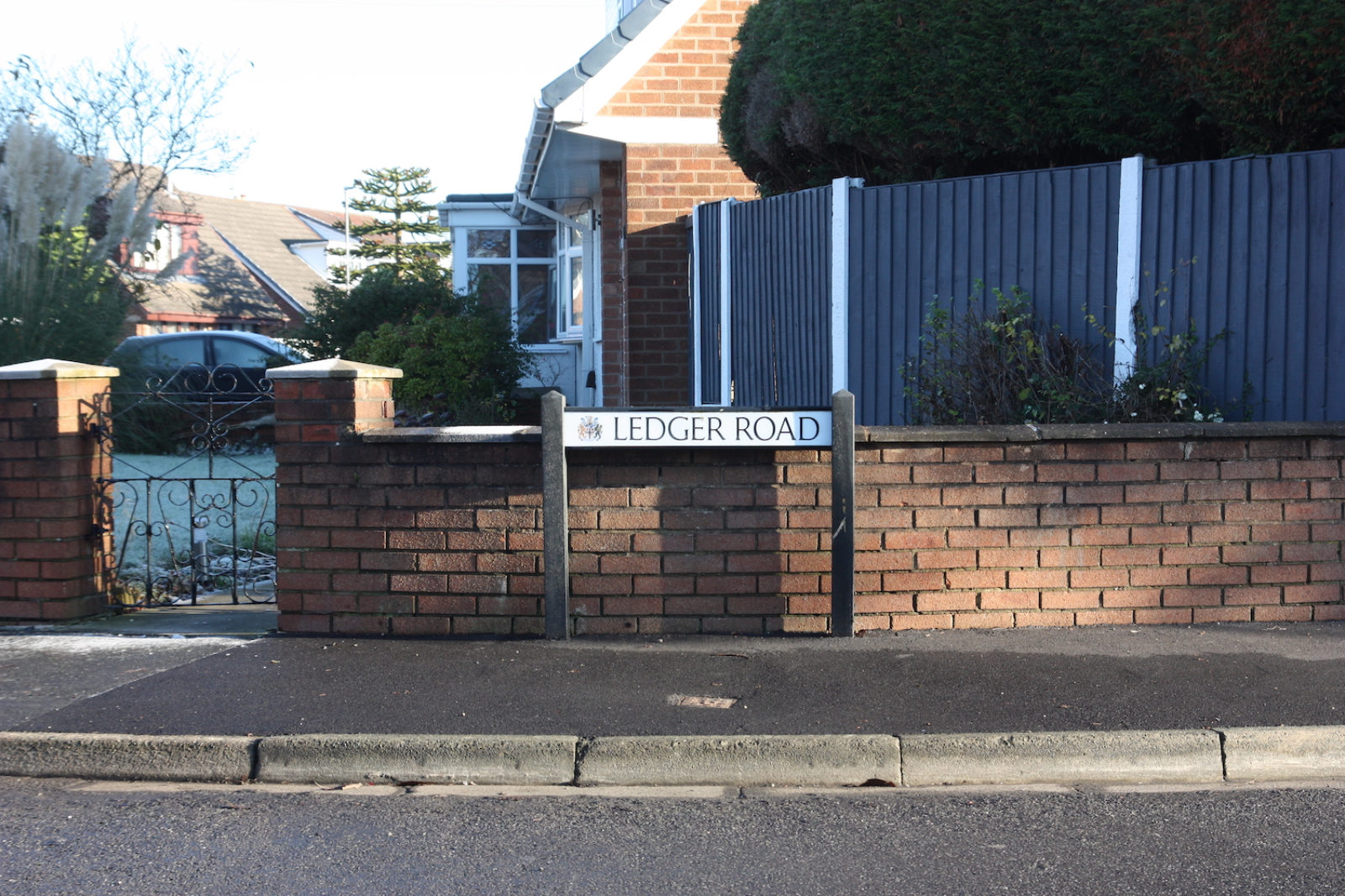 Ledger Road sign is in front of a half brick wall with a wrought iron gate leading to the front garden of a bungalow.