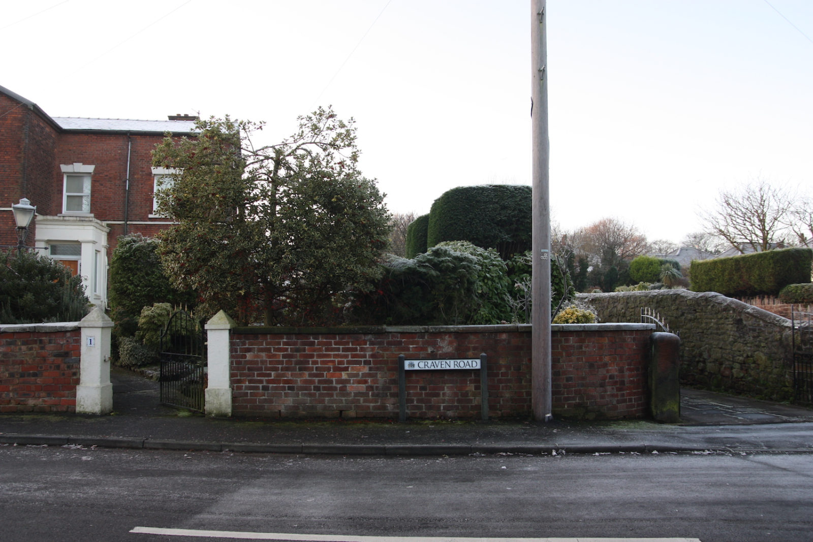 Craven Road sign is in front of a short brick wall which encloses a front garden full of trees and hedges.