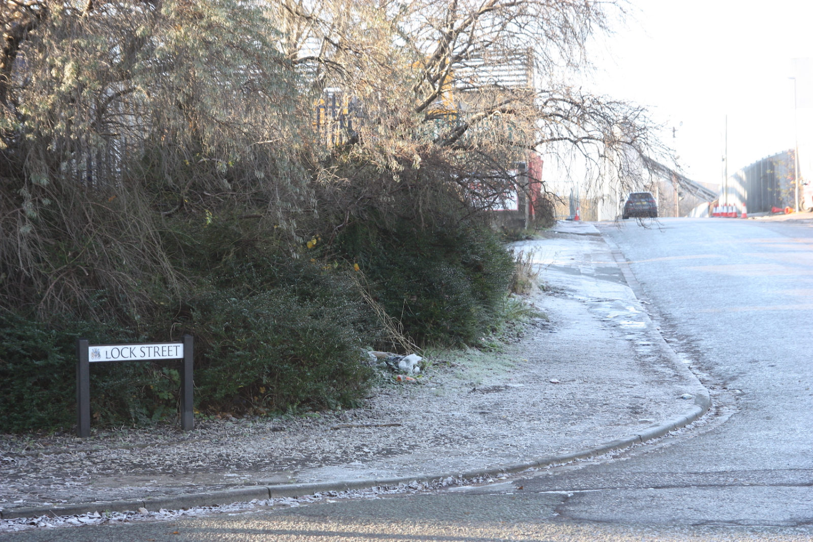 Lock Street is photographed on a frosty day, the sign is on a street corner and there are bare trees and railings in the background.