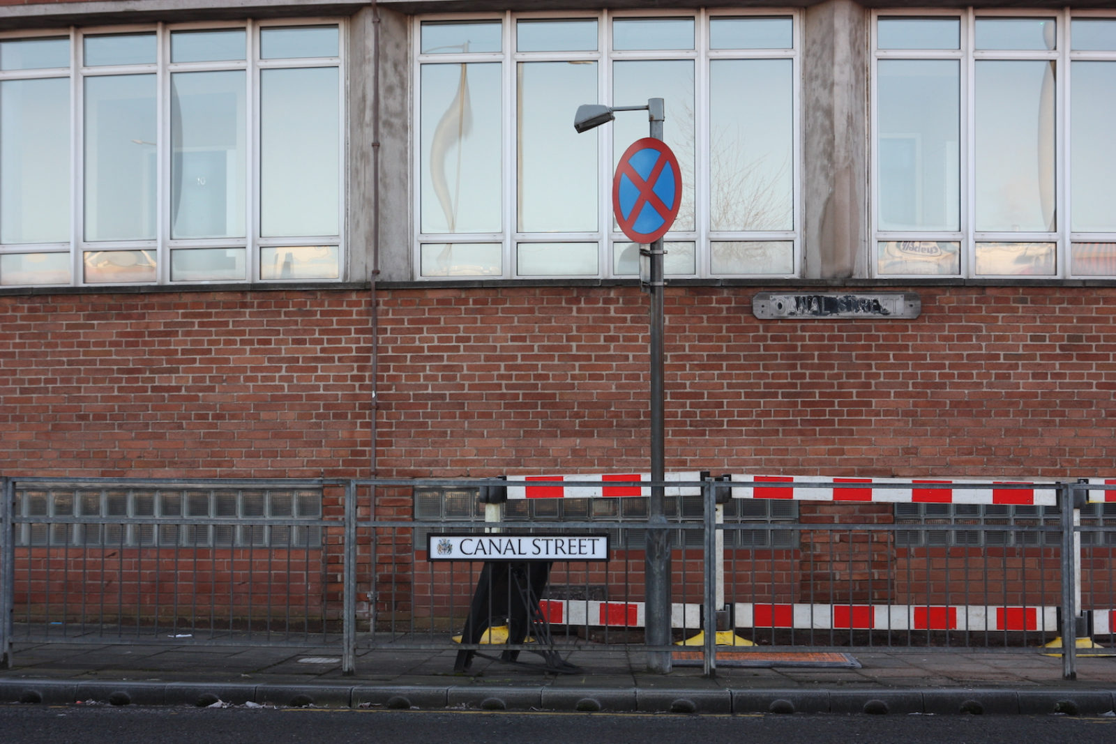 Canal Street Sign is on a metal railing in front of a no stopping sign. There is a red brick building with tall windows in the background.