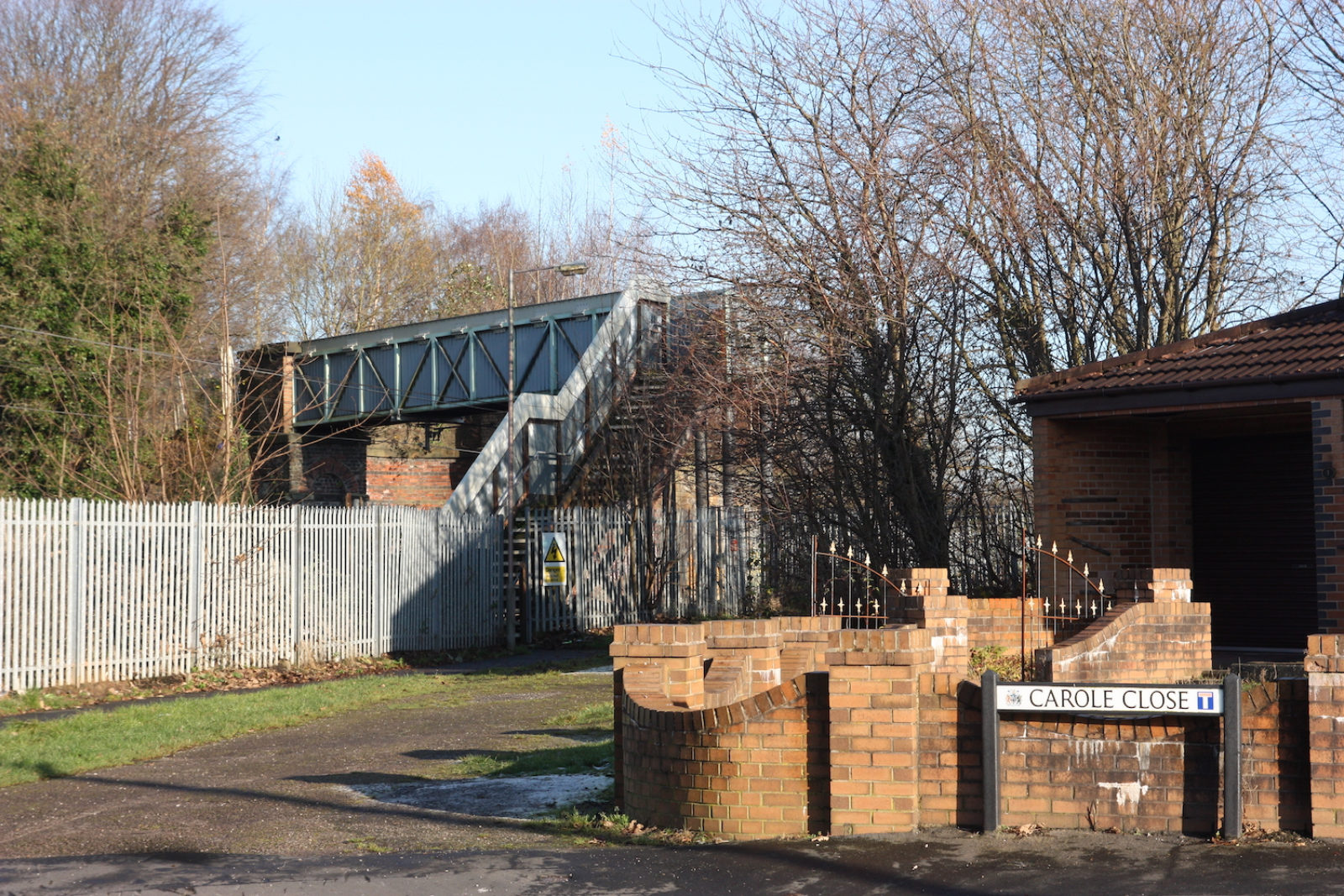 Carole Close Street sign, there are bare winter trees behind it and a train station bridge.