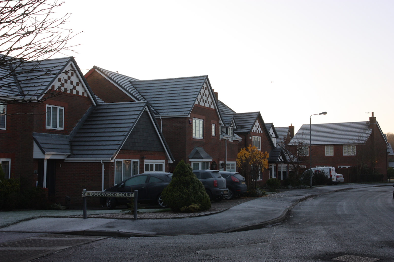 Goodwood Court sign is in front of a street of detached red brick houses.