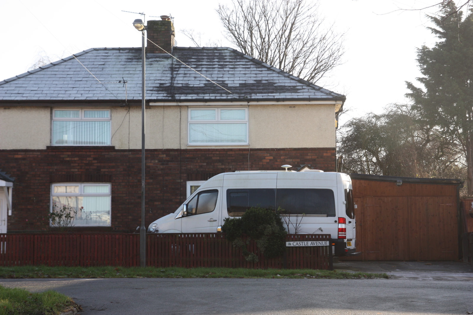 Castle Avenue sign is in front of a short brown wooden fence with a white van parked behind it and a house.
