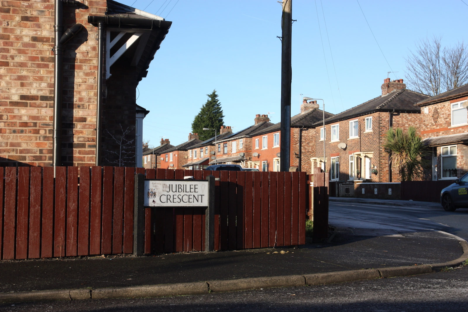 Jubilee Crescent sign is on a street corner in front of a fence painted brown.