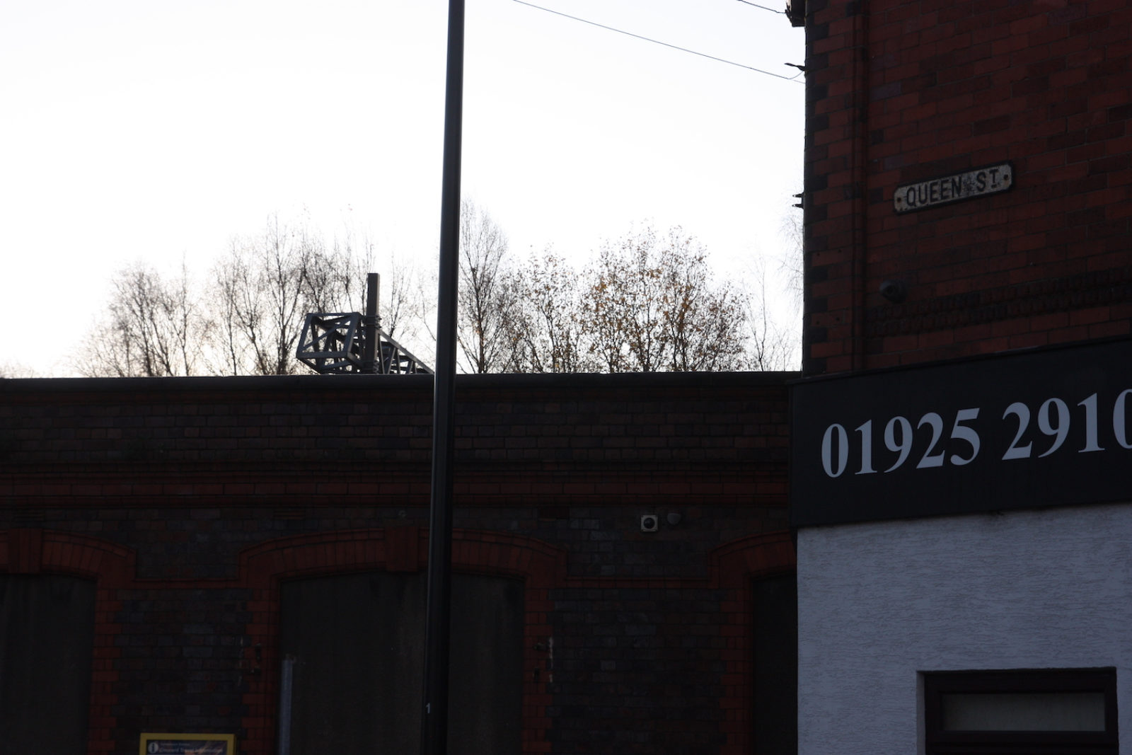 Queen St sign is fixed to a red brick wall above a shop sign.