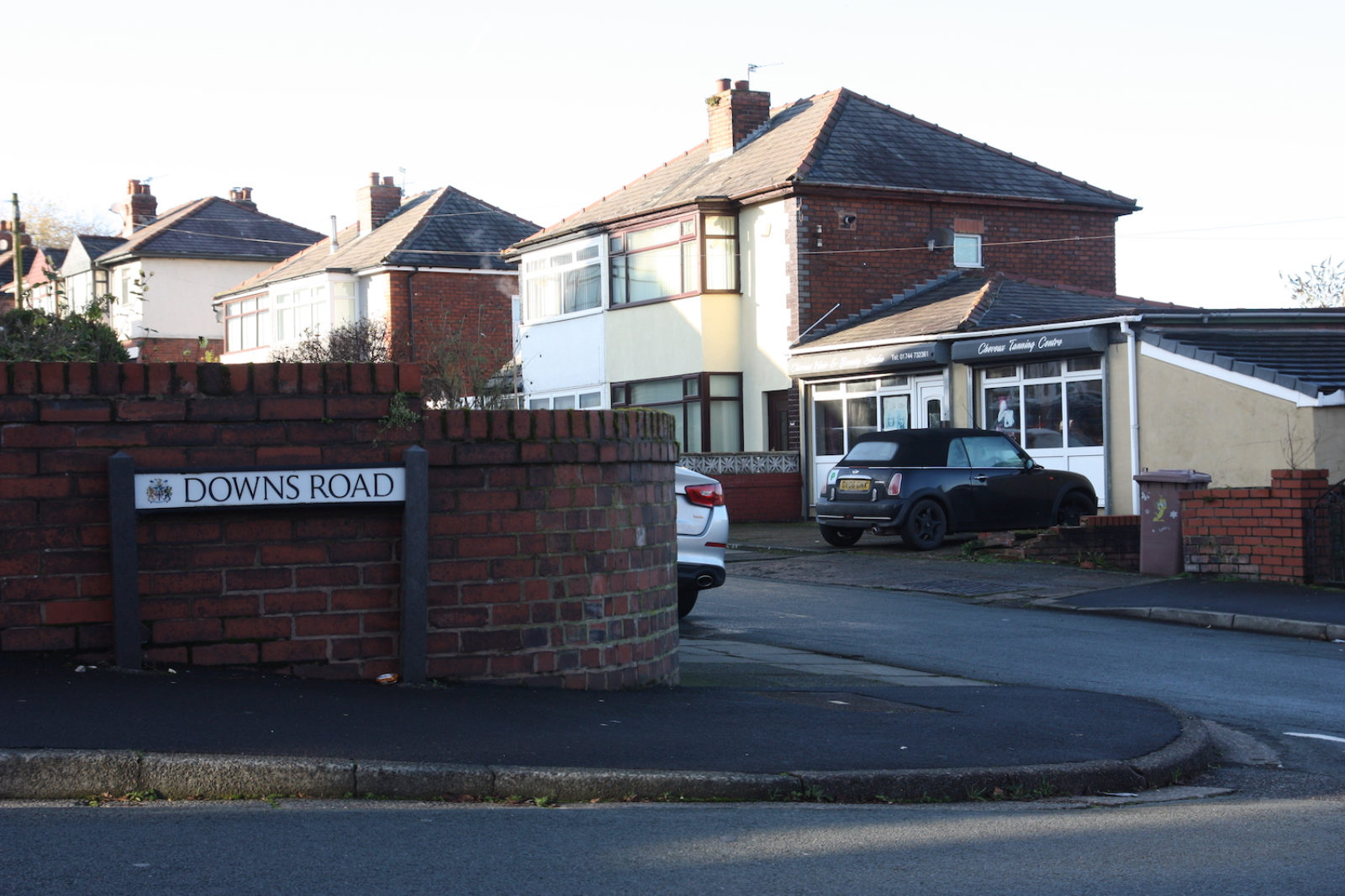 Downs Road sign is on a rounded red brick wall.
