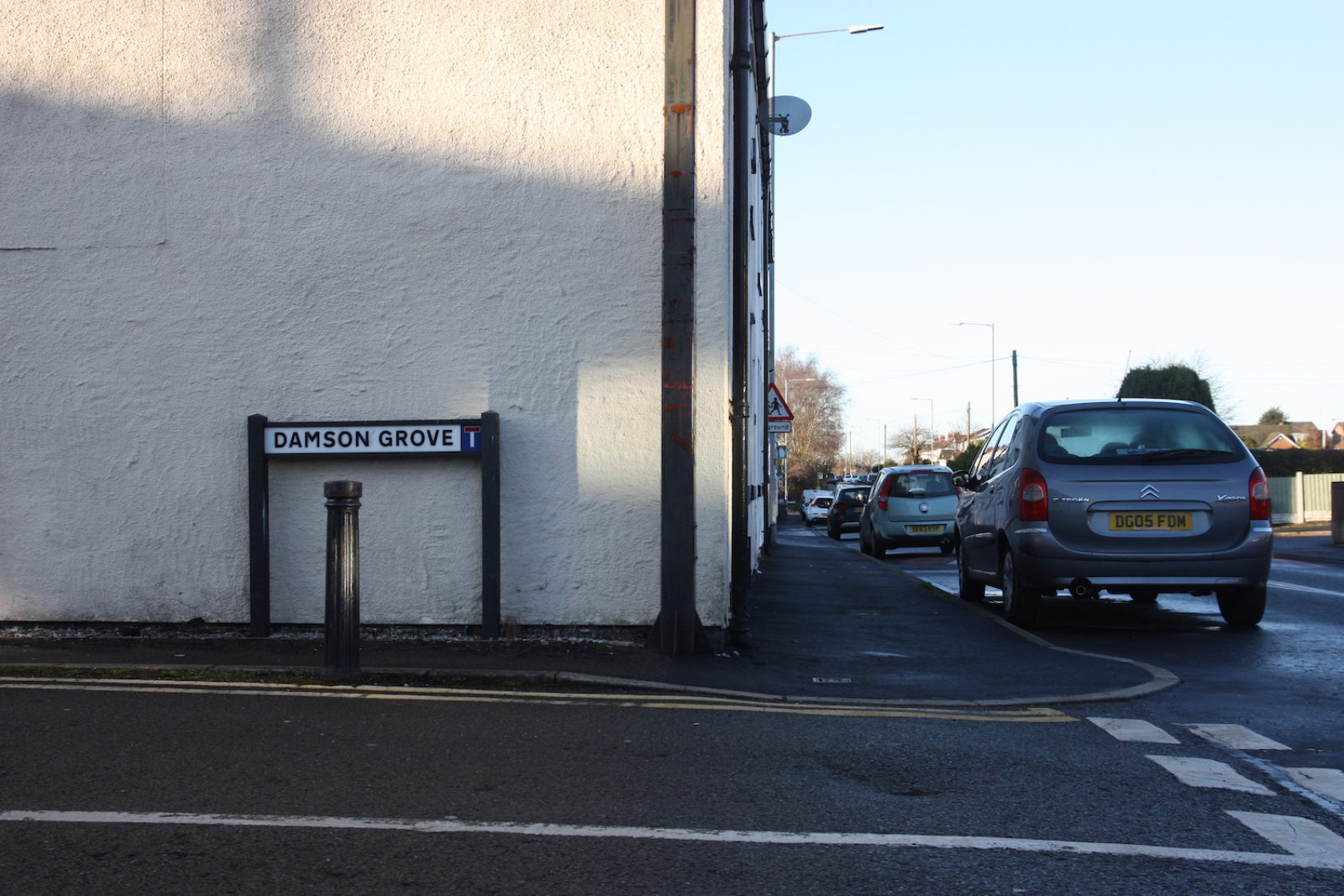 Damson Grove sign is on the side of a White House at the end of a street, there are cars parked on the road adjacent.