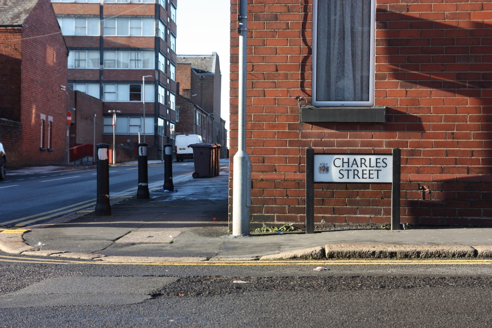 Charles Street sign is on a street corner in front of a red brick wall and a window, there is a tower block on the street adjacent and it is a sunny winter day.