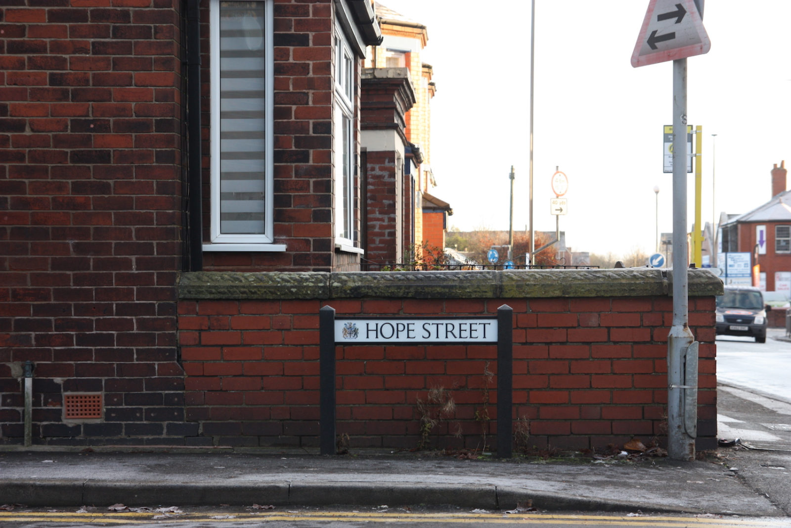 Hope Street sign is in front of a red brick wall of an end terrace's front garden,