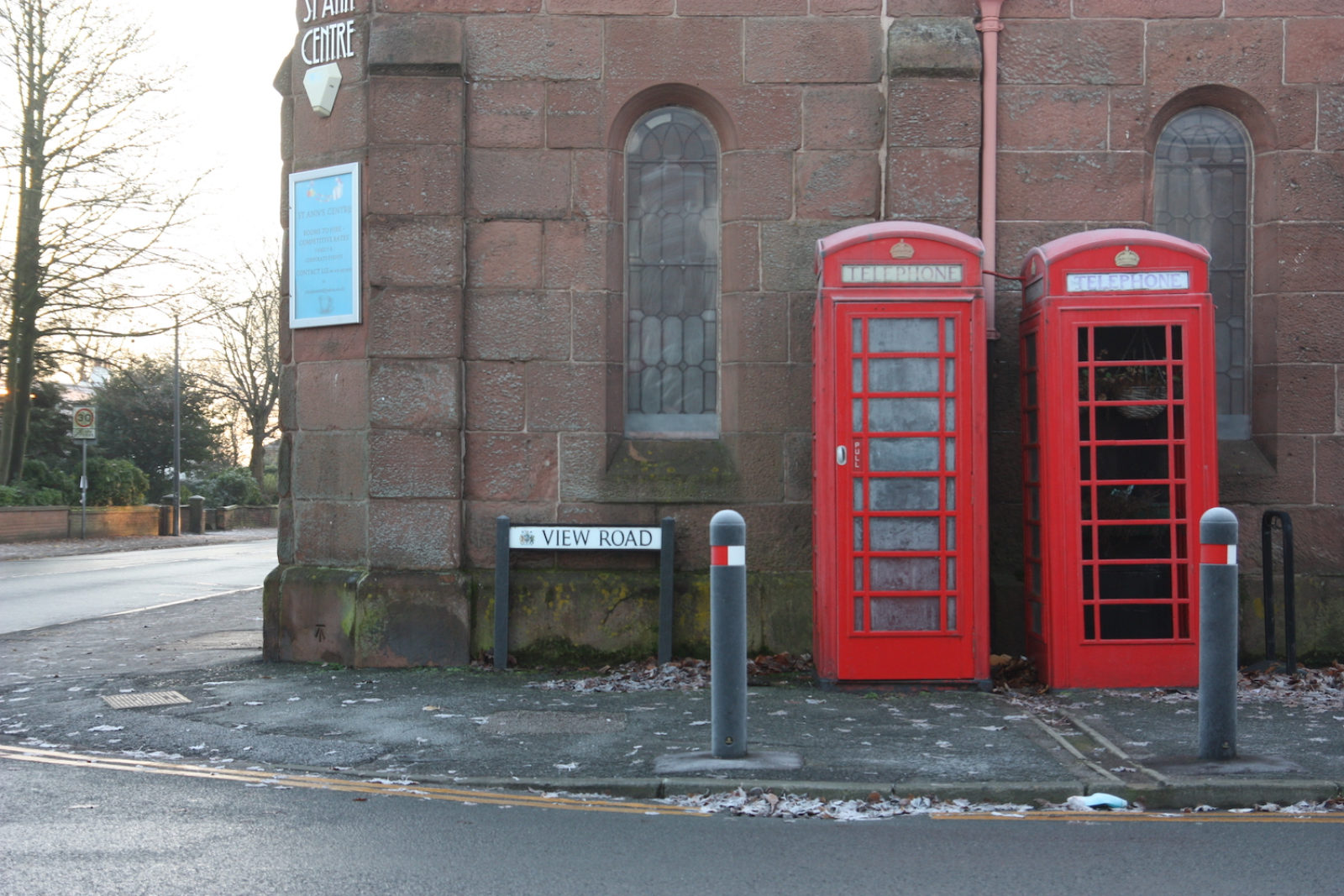 View road sign is outside a church next to two red telephone boxes. There are frosty leaves on the pavement.