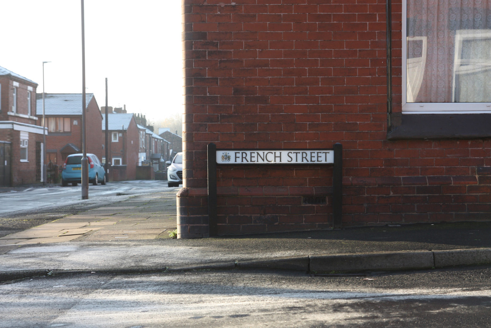 French Street is on the corner of a red brick house, the road in front of it is frosty.