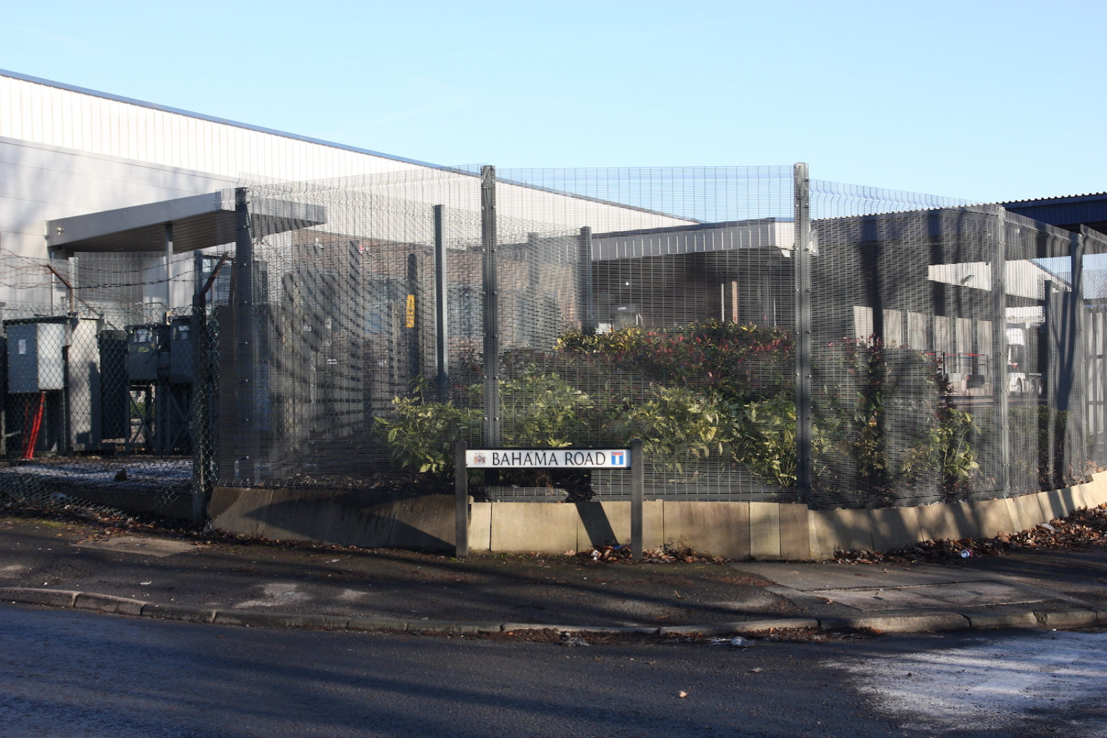 Bahama Road sign is in front of a tall wire fence in front of an industrial estate.