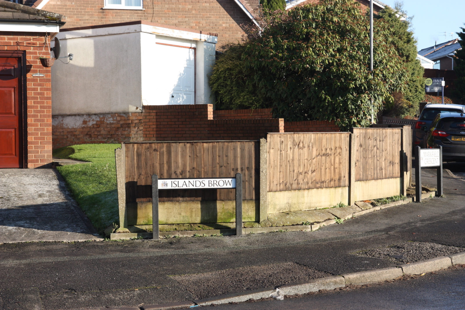 Islands Brow street sign is in front of a fence and two garages.