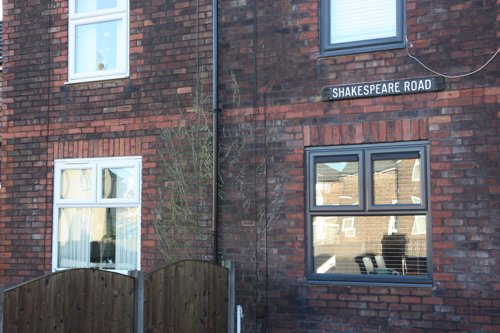 Shakespeare Road sign is old fashioned and is black with white letters, fixed to the wall of a red brick house.