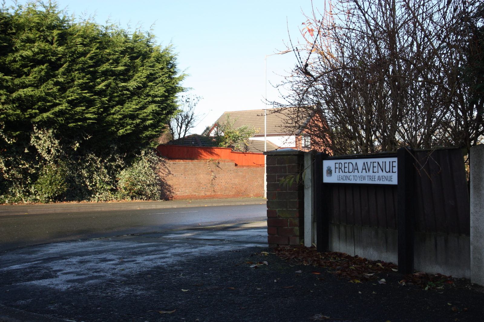 Freda Avenue leading to Yew Tree Avenue sign is photographed on at the end of the street in front of a fence with trees in the background.