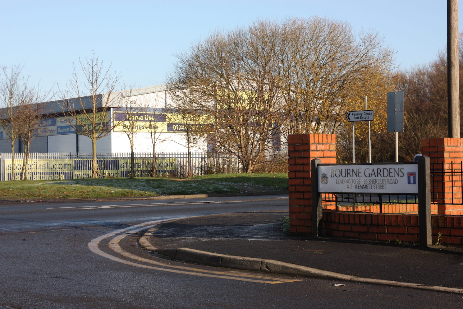 Bourne Gardens sign is on the corner of a street and in the background is an industrial estate.