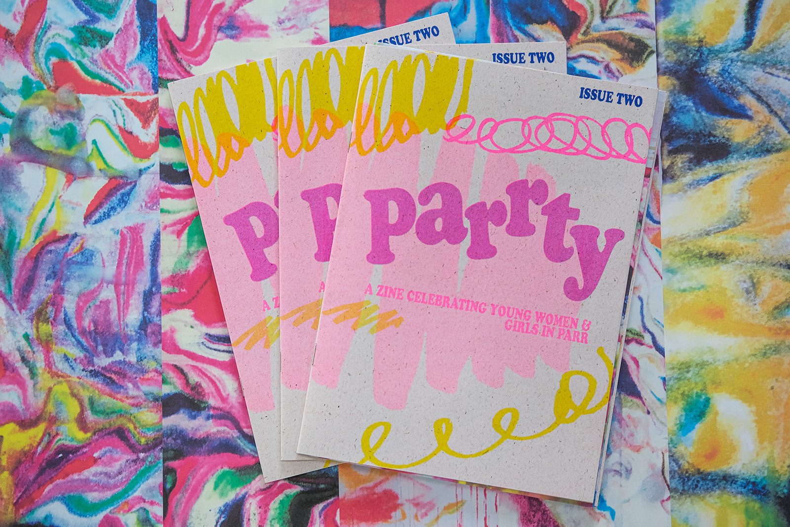 A fanned spread of issue two of PARRTY printed in popping colours of fluorescent pink, blue and yellow.