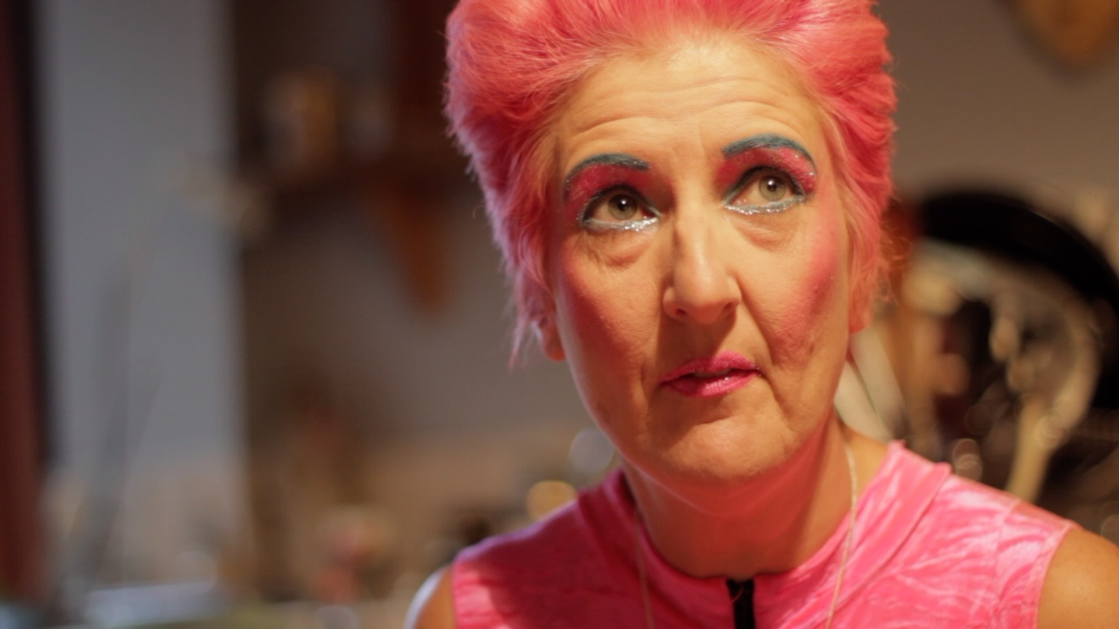 Close up photograph of Kitty O'Shea with pink hair, wearing pink eyeshadow and a pink top, looking up above the camera.