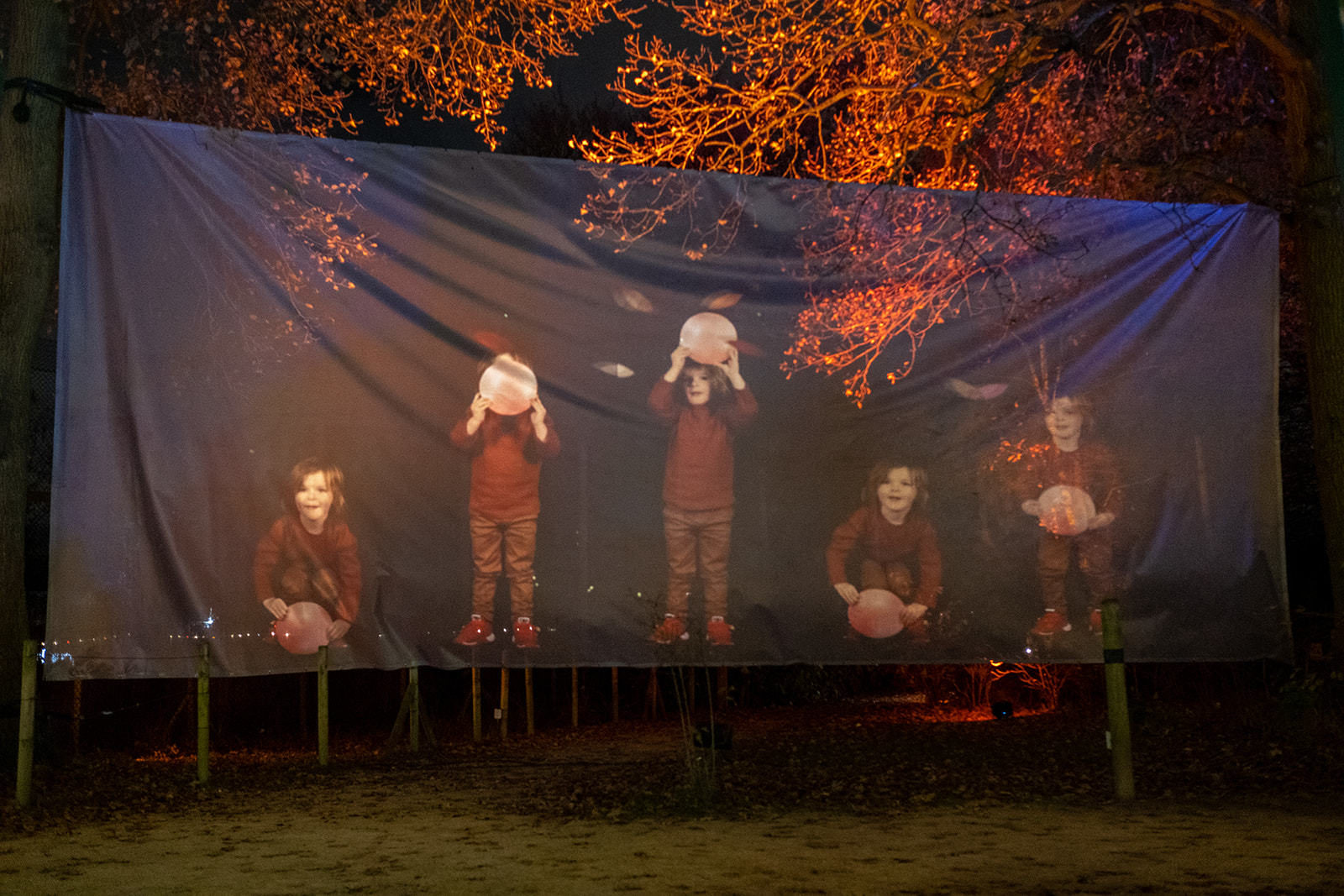 A huge piece of fabric hangs between trees. On it is projected a series of images of a small child holding up a moon.