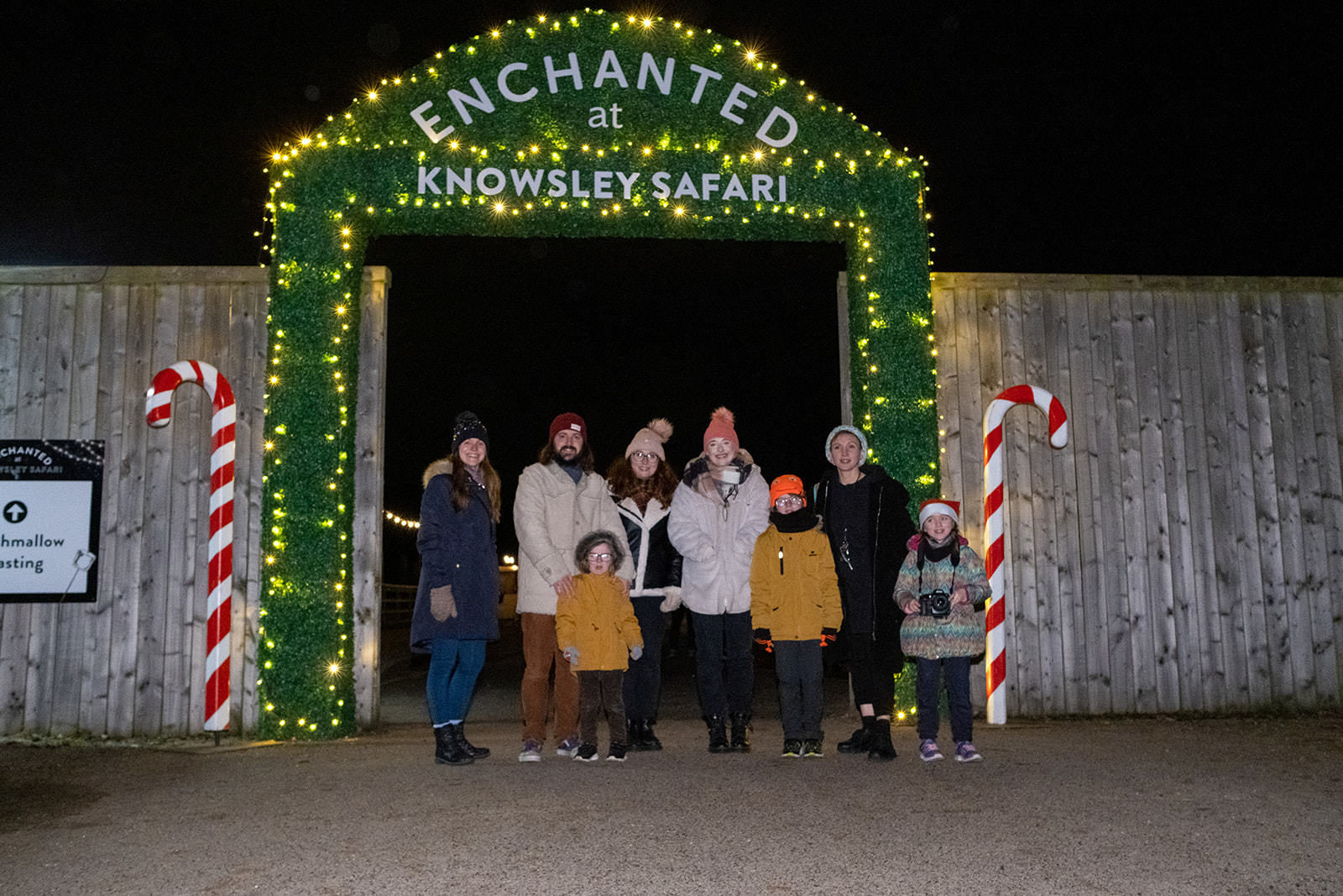 A group of people in woolly hats stand under a entrance that reads "Enchanted at Knowsley Safari"
