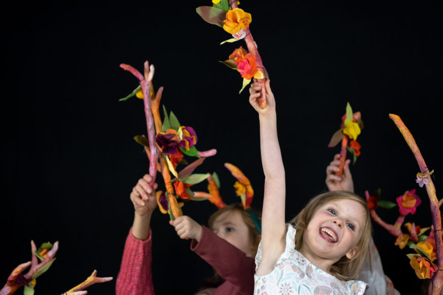 Children holding hand made floral antlers in the air, smiling.