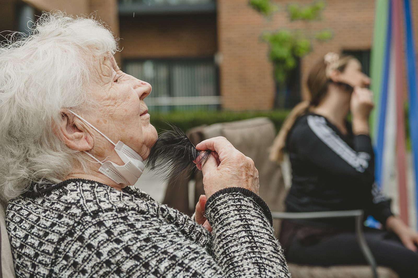 An elderly woman strokes her face with a black feather.