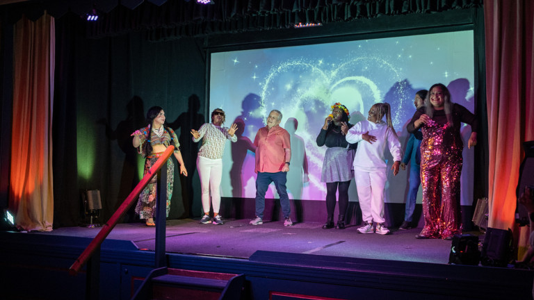 A group of people stand on a stage singing in front of a large screen