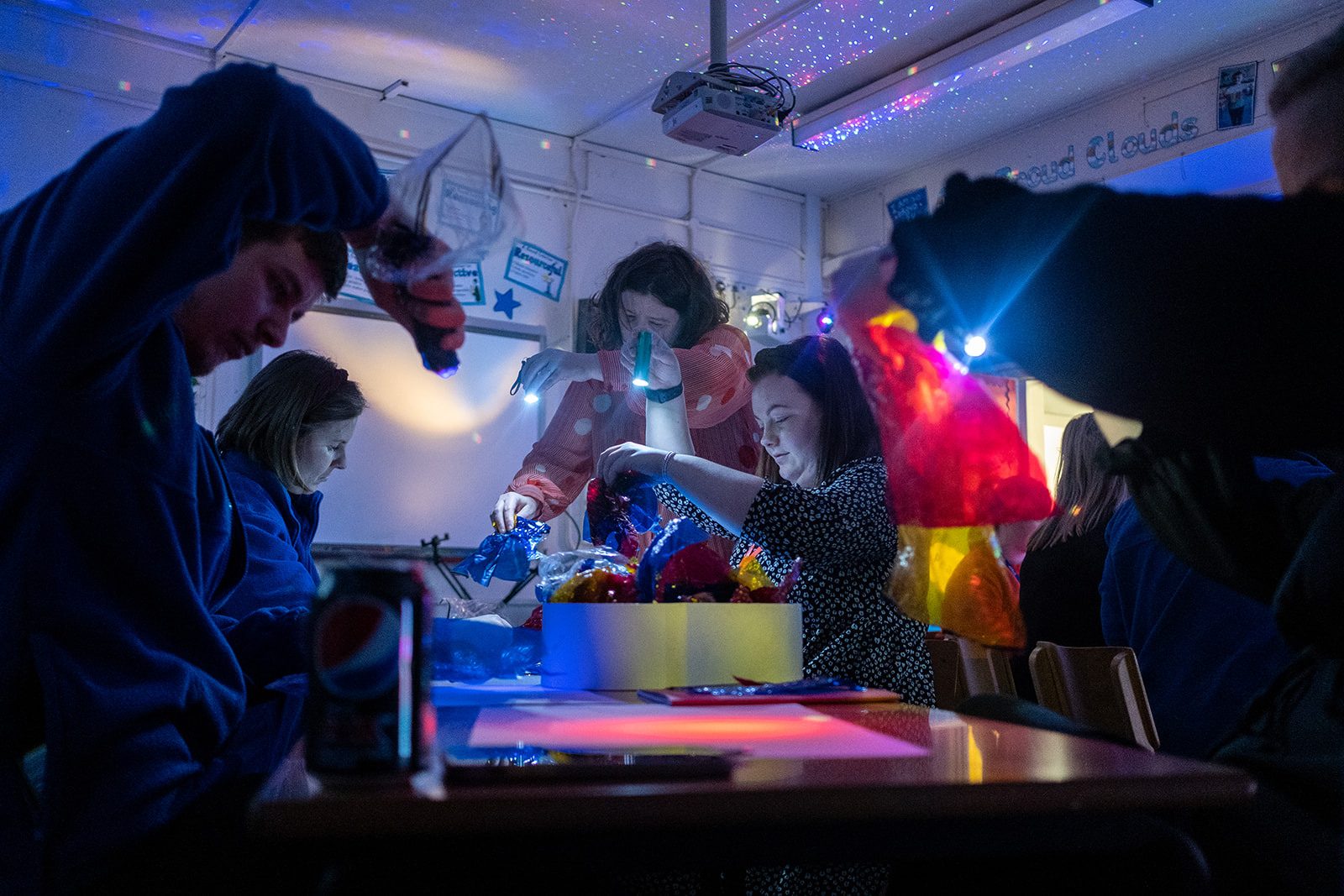 In a slightly darkened room with lights projected on the ceiling like a starry night teachers are sitting at a table illuminated by torch light. They are making interesting objects and projections with colourful plastics. Artist Cathy Cross stands at the end of the table demonstrating what can be done.