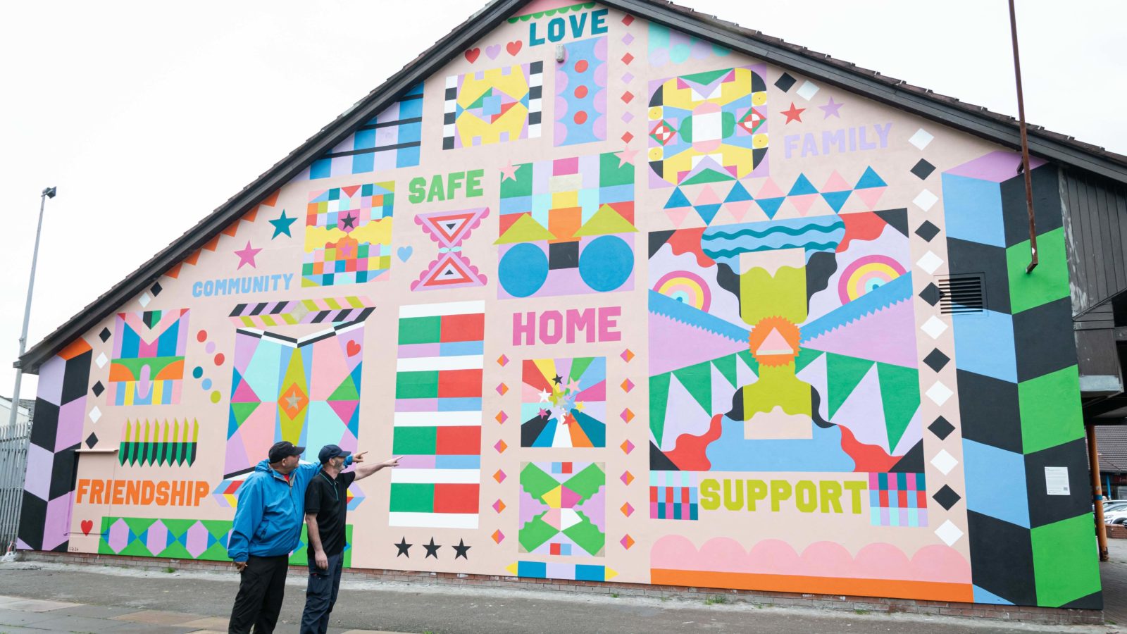 Two men are photographed pointing in unison at the mural and looking at it. They are both smiling.