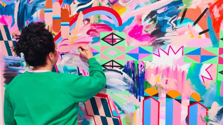 Cherie is photographed wearing a bright green jumper and leopard print leggings, working on a large abstract painting.