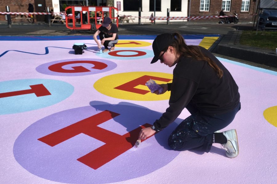 Two people painting a bold colourful mural on the ground.