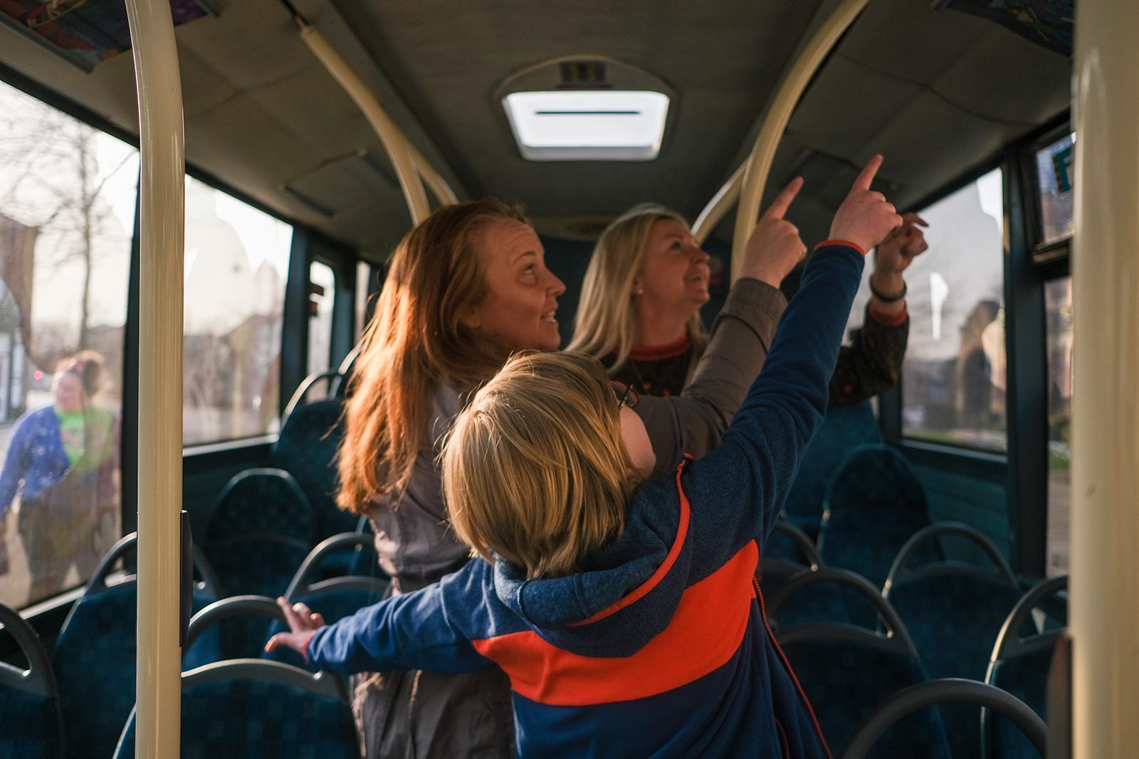 Three people stand inside a bus looking up at the internal panels and smiling.