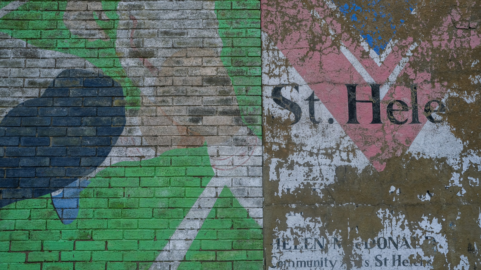 Close-up of an old mural. Paint flakes off the brickwork and the original image has faded.