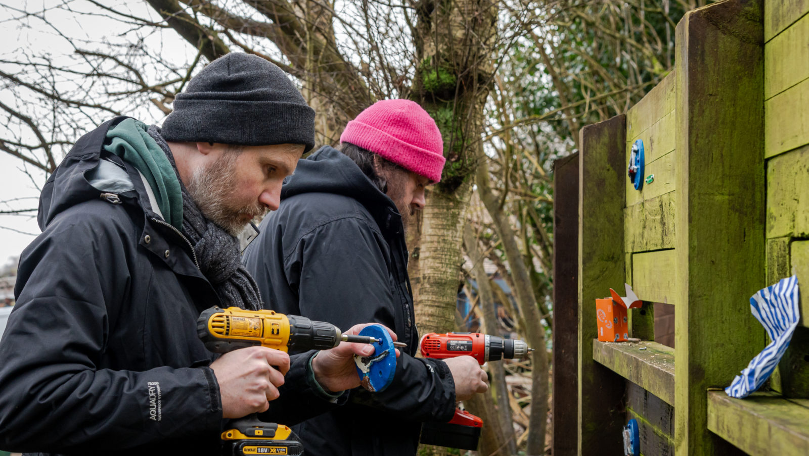 Photograph of two men drilling small ceramic tiles into a fence