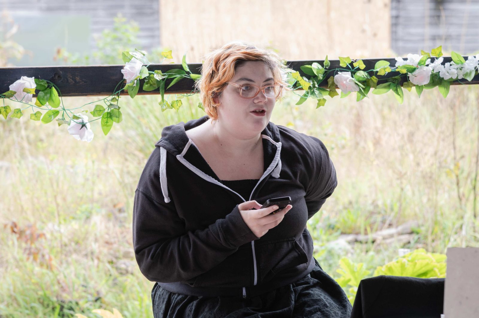 A participant of John Maguire's Parklife workshops reads a poem off their phone in incredible edible community garden.