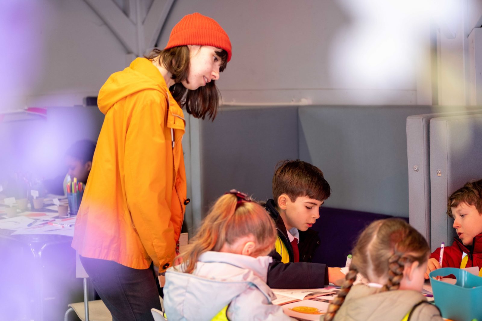 Cath facilitates as children sit around tables using coloured pens to fill in their zines