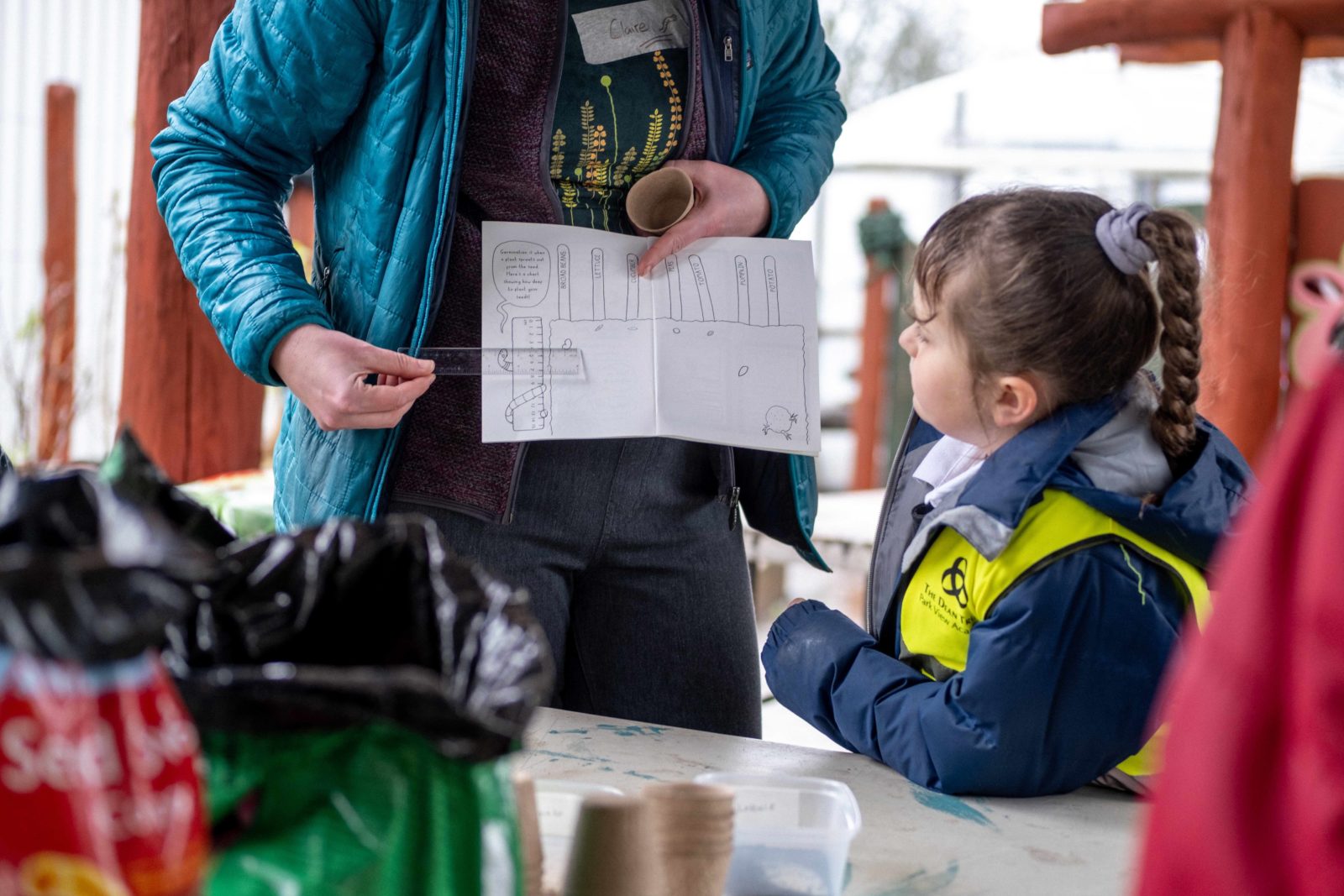 A woman holds a ruler up to the zine, talking a schoolchild through it.