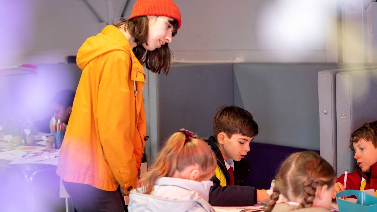 Cath facilitates as children sit around tables using coloured pens to fill in their zines