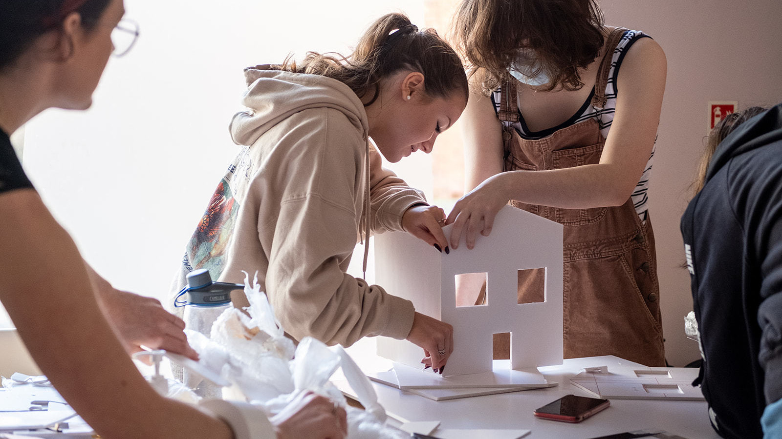 Two young women build a model of a house together from cardboard