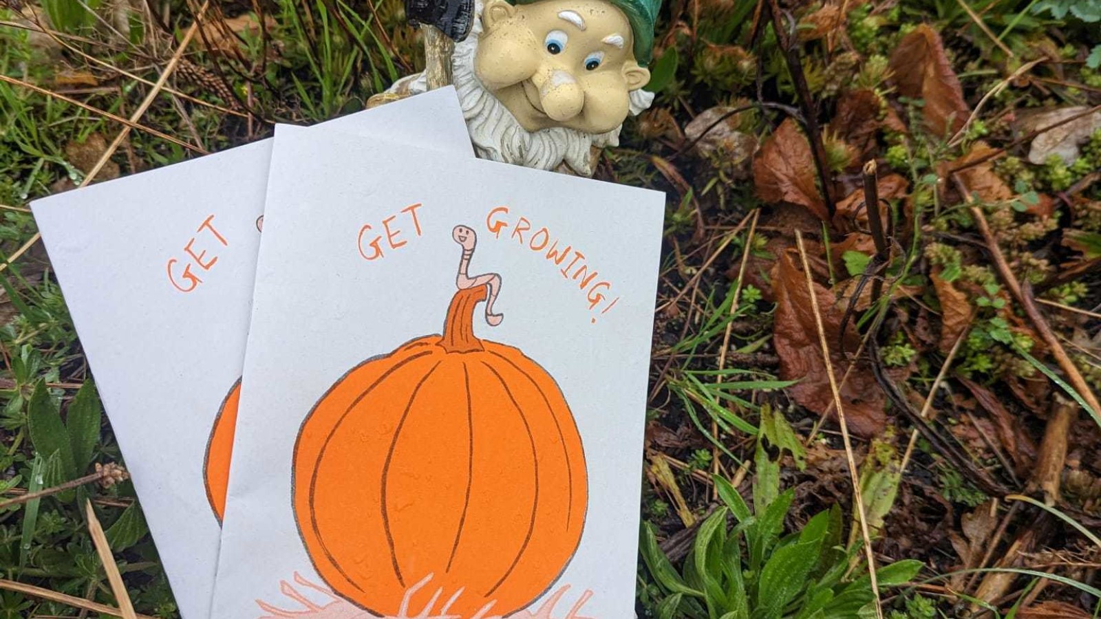 A garden gnome holds a small handmade comic with a pumpkin on the front
