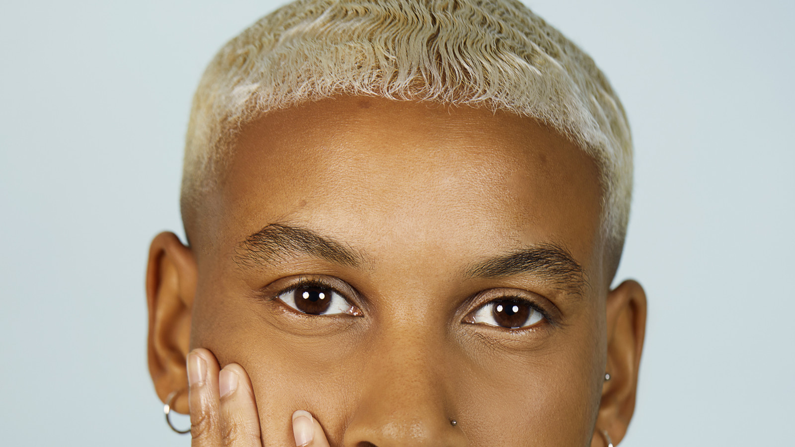 Kei is a Black person with bleached blond, cropped hair. They wear silver jewellery and a pastel green t-shirt.