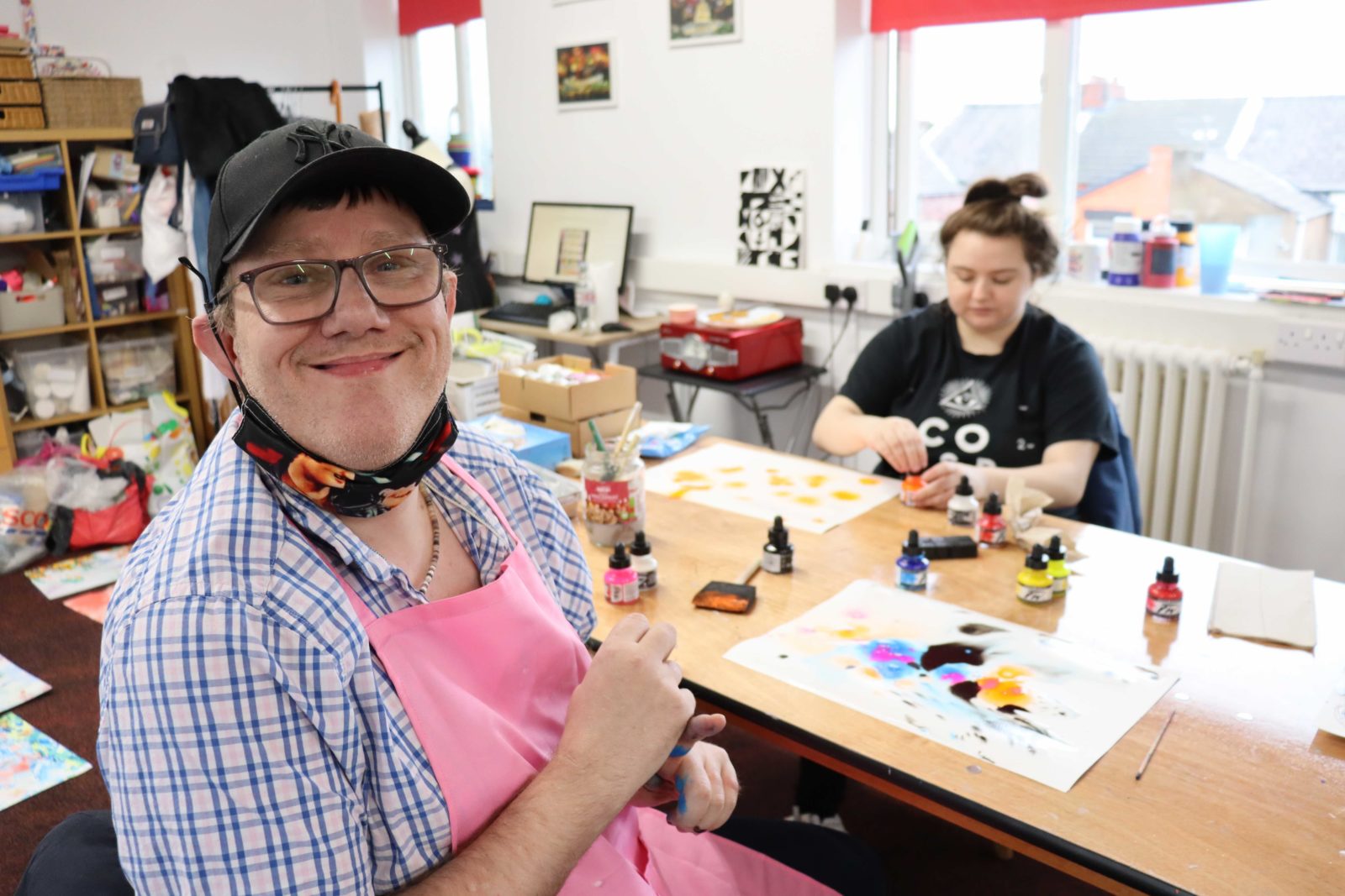 2 buzz hub members participate in the workshop, one is smiling at the camera and the other is working in the background, they are using inks to create marbling.