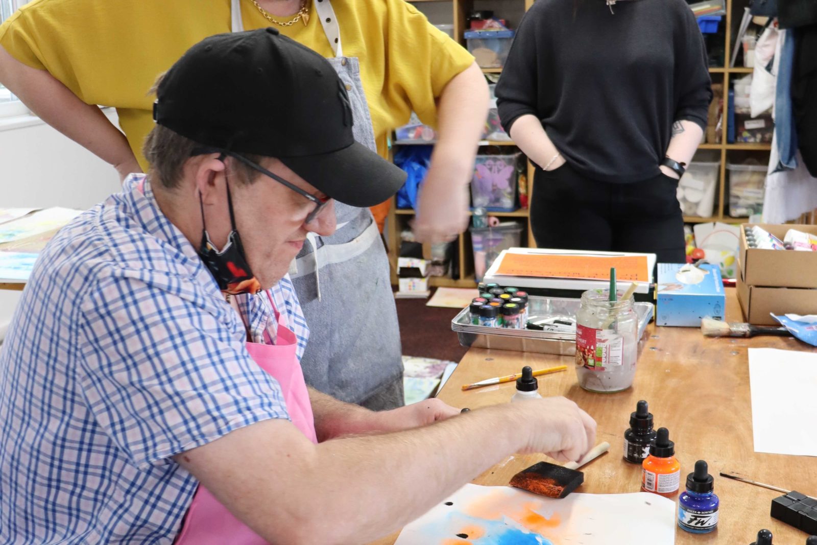A buzz hub member working on a marbling piece with inks, two women are smiling whilst watching him work.