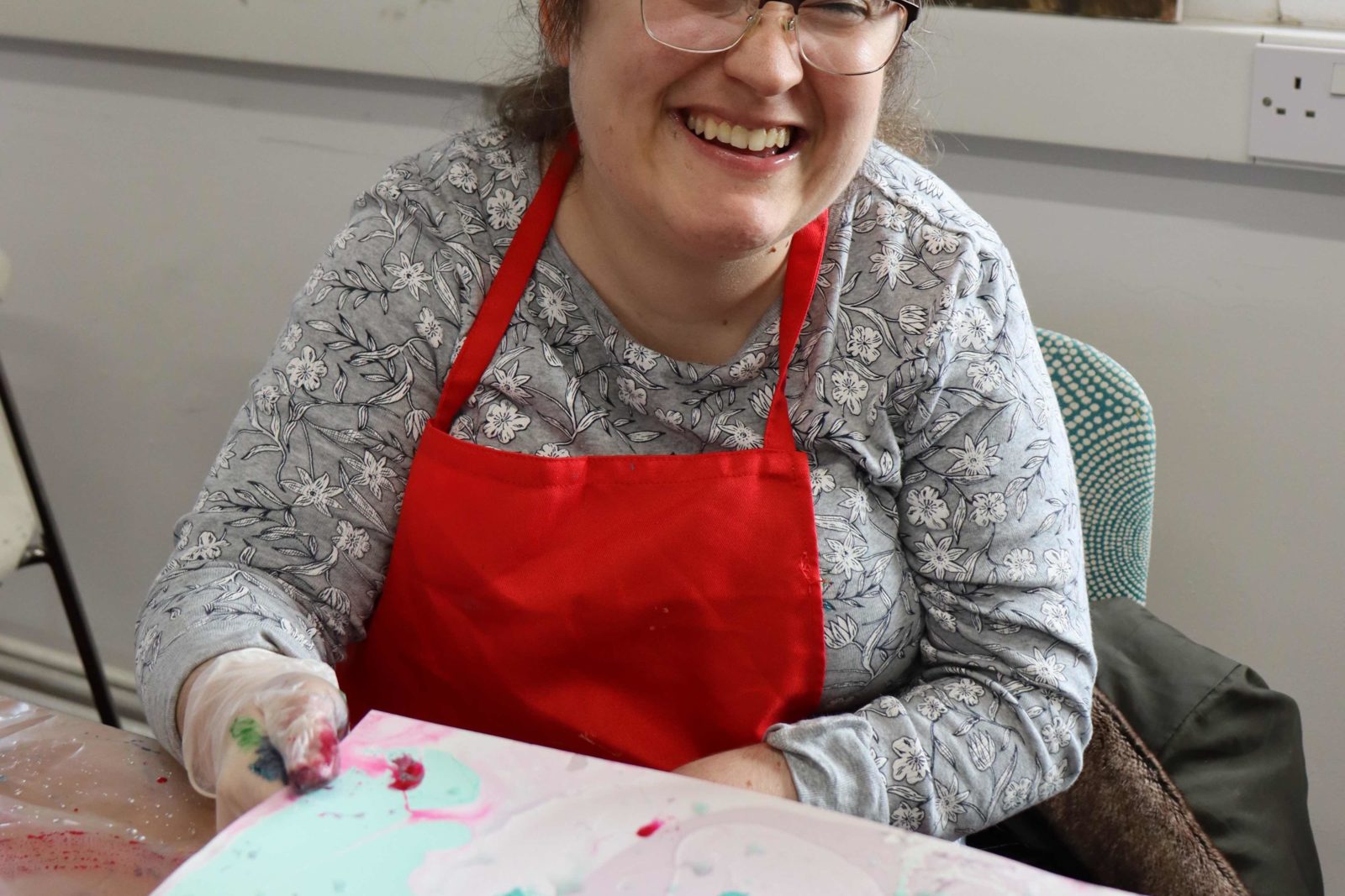 A Buzz Hub member holding her marble painting in a gloved hand, smiling at the camera and wearing a red apron.