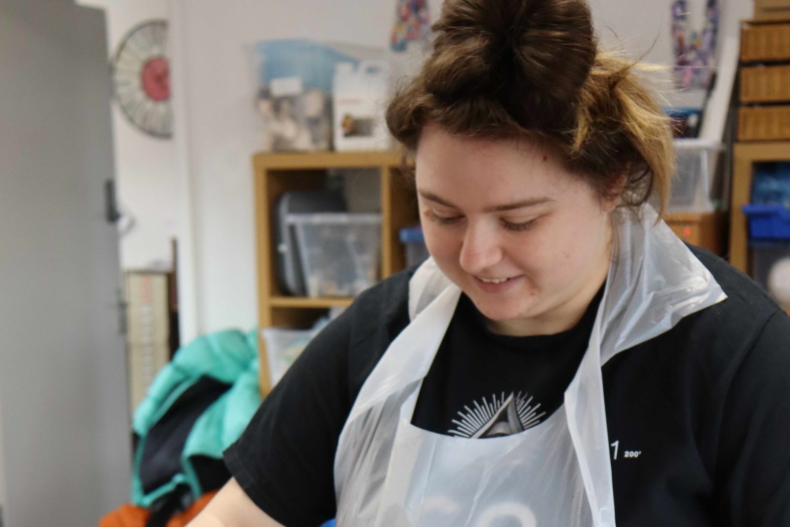 A Buzz Hub member in a plastic apron and plastic gloves holding a piece of card in a tray of ink to create a marble painting.