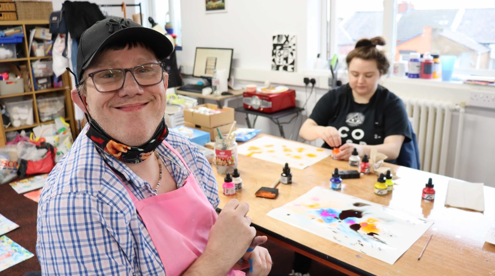 2 buzz hub members participate in the workshop, one is smiling at the camera and the other is working in the background, they are using inks to create marbling.