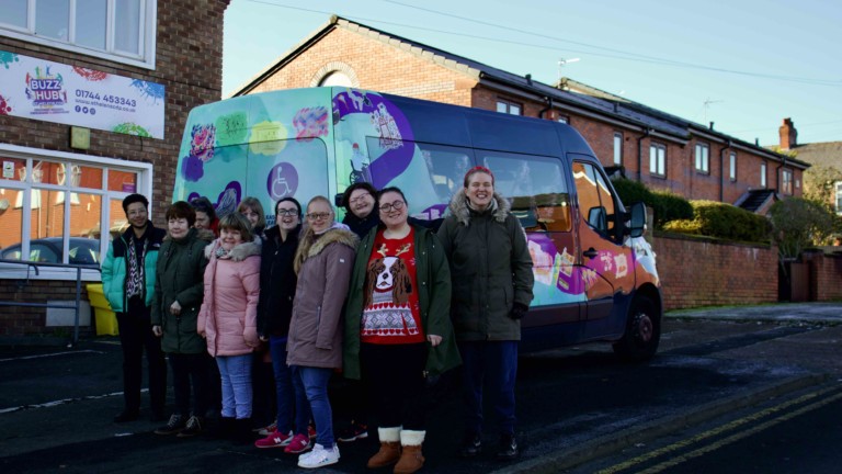 Buzz Hub members standing with Rudy in front of the bus, smiling at the camera on a sunny winter morning.