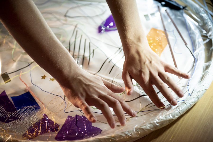 An abstract design is shown on a piece of clear plastic. A person's hands are pushing some plastic down on to the design.